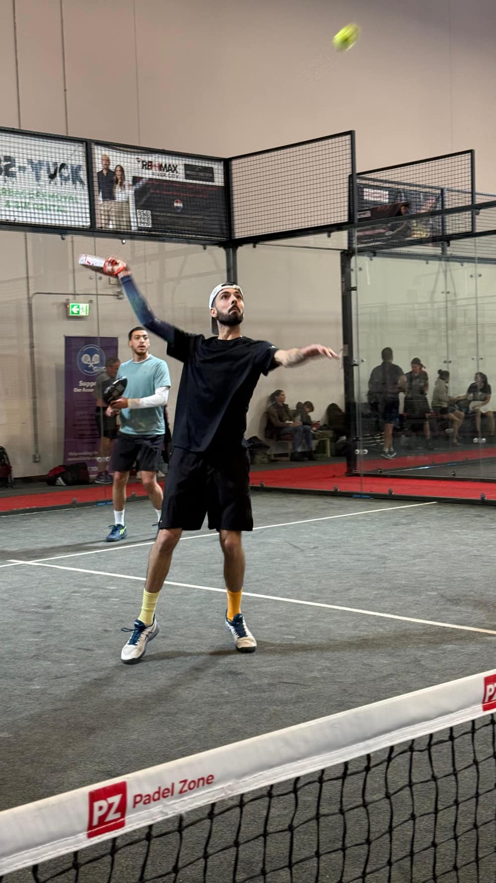 A member serving mid-point on the padel court
